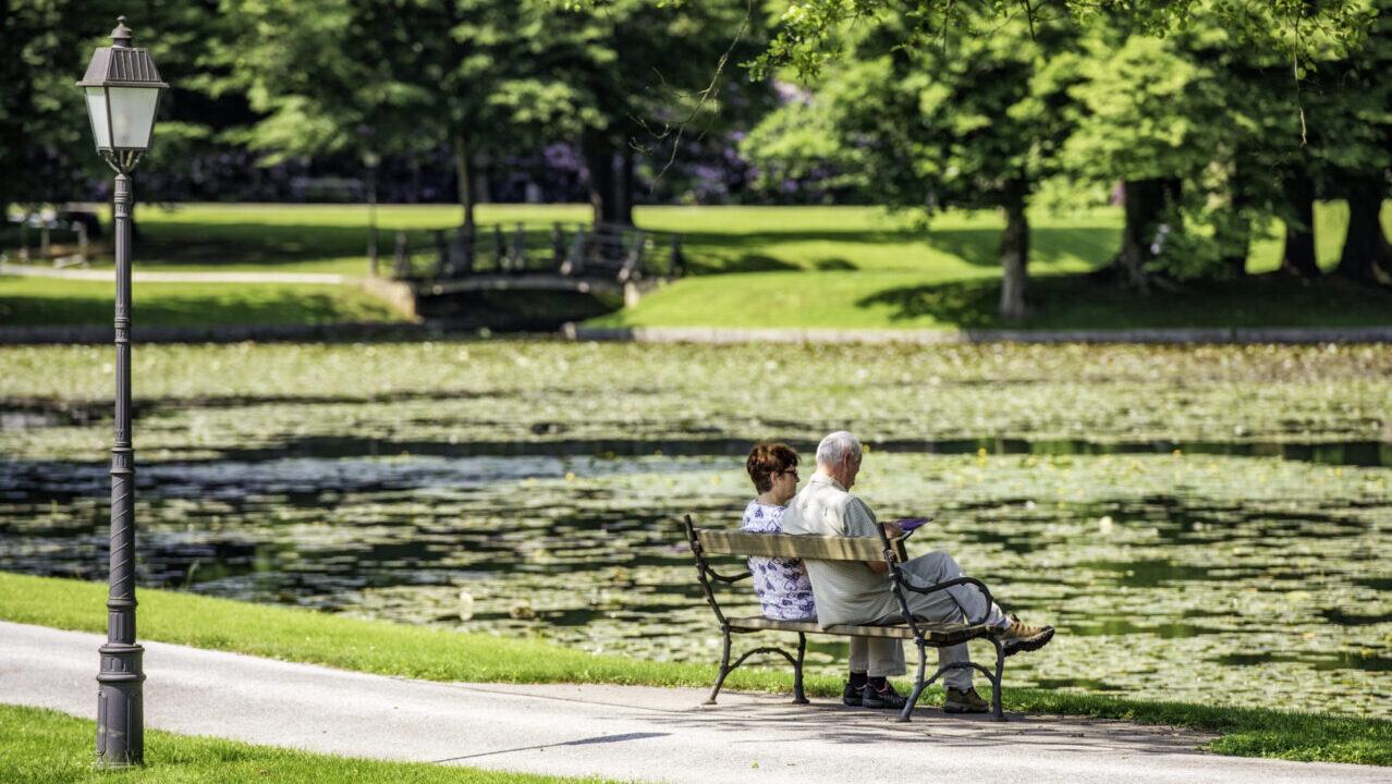 Verde urbano, qualcosa è cambiato: una coppia di anziano in un parco davanti a un laghetto
